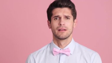 Papyon takan ciddi bir genç adam, stüdyodaki pembe bir duvarın arkasında duran negatif duygularla parmağını sallıyor.