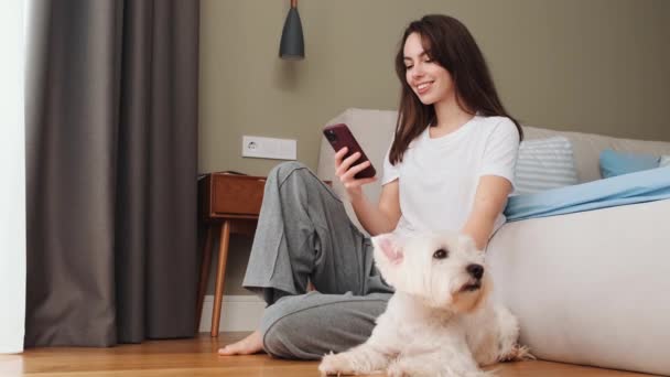 Happy Girl Petting Her Dog While Using Her Smartphone Sitting — ストック動画