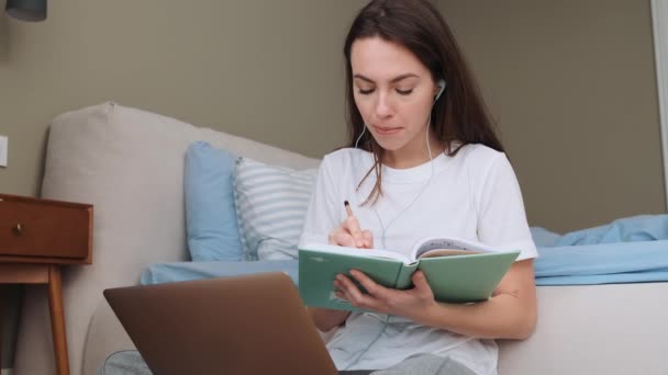 Een Gefocuste Vrouw Maakt Aantekeningen Terwijl Haar Laptop Slaapkamer Thuis — Stockvideo