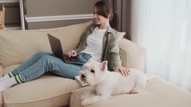 Cheerful Girl Petting Her Dog While Using Her Laptop Sitting — ストック動画