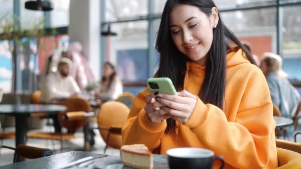 Die Lächelnde Frau Einem Orangefarbenen Kapuzenpullover Sucht Etwas Telefon Während — Stockvideo