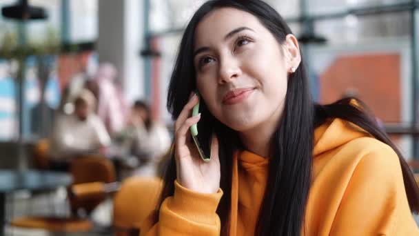 一个穿着橙色帽衫的积极女子坐在咖啡店里 一边打电话一边正面摇着头 — 图库视频影像
