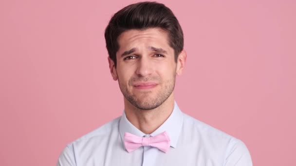 一位戴着蝴蝶结领带的心怀不满的年轻人站在工作室的粉红墙上做着一个脸 掌的手势 — 图库视频影像