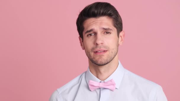 一个戴着蝴蝶结领带的严肃的年轻人站在演播室的粉红墙上做着 别跑得那么快 的手势 — 图库视频影像