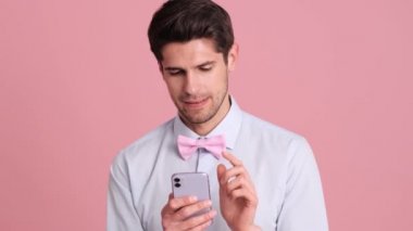 Papyon takan ciddi bir genç, akıllı telefonunu stüdyodaki pembe bir duvarın arkasında tek başına duruyor.