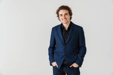 Ceketli neşeli yakışıklı adam gülümsüyor ve beyaz arka planda izole edilmiş kameraya bakıyor.