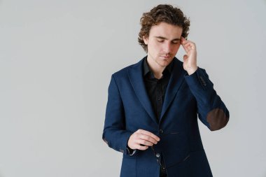 Beyaz arka planda gözlük tutan yorgun ve yakışıklı bir adam.