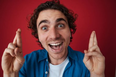 Heyecanlı kulaklıklı yakışıklı adam kırmızı arka planda parmaklarıyla poz veriyor.