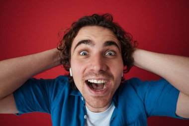 Heyecanlı kulaklıklı yakışıklı adam kırmızı arka planda mahsur kalmış kameraya şaşırdığını söylüyor.