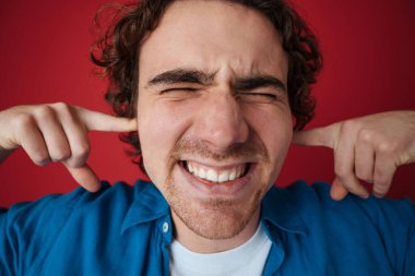 Stresli yakışıklı adam kulaklarını tıkarken yüzünü buruşturuyor.