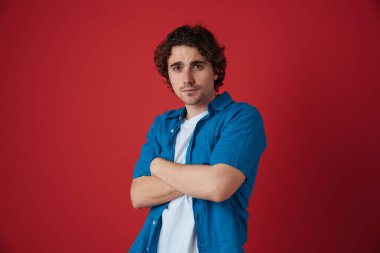 Beyaz, yakışıklı, kolları çaprazlanmış bir adam kırmızı arka planda izole edilmiş.