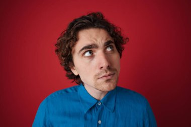 Düşüncelere dalmış yakışıklı bir adam kırmızı arka planda izole edilmiş bir şekilde düşünüyor ve bakıyor.