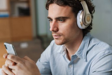 Ofiste çalışırken cep telefonuyla kulaklık takan Kafkasyalı genç iş adamı.