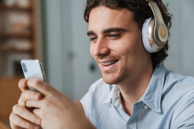Ofiste çalışırken cep telefonuyla kulaklık takan Kafkasyalı genç iş adamı.