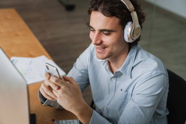 Ofiste çalışırken cep telefonuyla kulaklık takan Kafkasyalı genç iş adamı.