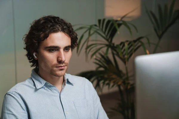 オフィスでコンピュータ上で働くイヤホンの白人の若い重大なビジネスマン — ストック写真