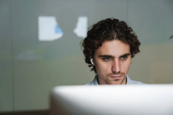 オフィスでコンピュータ上で働くイヤホンの白人の若い重大なビジネスマン — ストック写真
