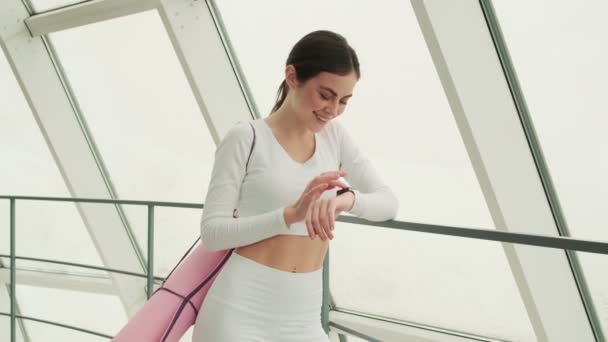 Die Positive Sportlerin Blättert Auf Einer Armbanduhr Während Sie Fenster — Stockvideo