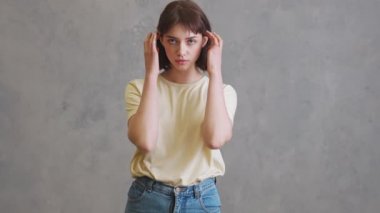 Gri stüdyoda dikilirken saçını düzelten kendine güvenen kısa saçlı kız.