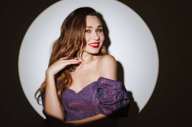 Güzel, heyecanlı, çekici bir kadın. Kokteyl elbisesi ve aksesuar giymiş. Sahne ışıkları altında poz veriyor.