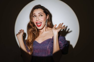 Güzel, heyecanlı, çekici bir kadın. Kokteyl elbisesi ve aksesuar giymiş. Sahne ışıkları altında poz veriyor.