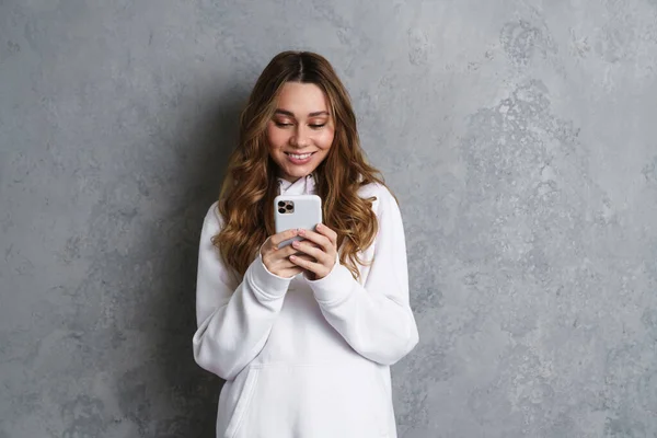 Portret Uśmiechniętej Swobodnej Kobiety Trzymającej Smartfona Szarym Tle Piszącej Smsy — Zdjęcie stockowe