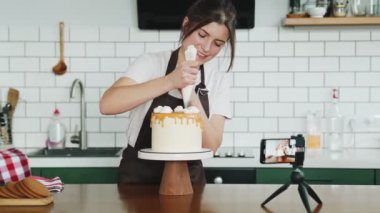 Olumlu bir pasta şefi kremalı güller yapıyor ve mutfakta kamerasına bir şeyler anlatıyor.