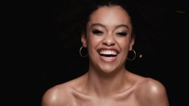 Güzel, şaşırmış bir Afrikalı Amerikalı kadın kameraya bakıyor. Stüdyodaki siyah arka planda tek başına dururken altın konfetileri düşüyor.