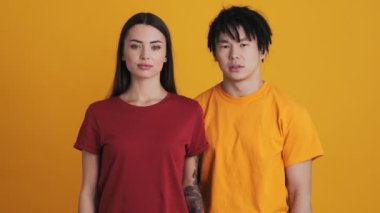 Çok uluslu bir çiftten memnun olmayan erkek ve kadın, stüdyodaki sarı duvarın üzerinde tek başlarına başparmak hareketi yapıyorlar.