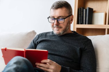 Memnuniyet veren, traşsız bir adam evdeki kanepede otururken notlar yazıyor.