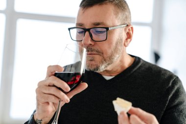 Evde şarap içip peynir yiyen konsantre olmamış yetişkin bir adam.