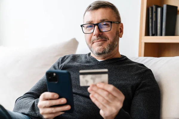 Evde Cep Telefonu Kredi Kartı Kullanan Gözlüklü Mutlu Tıraşsız Bir — Stok fotoğraf