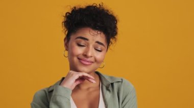 Rüya gören Amerikalı bir kadının yakın çekim görüntüsü stüdyodaki sarı duvarın üzerinde izole bir şekilde kameraya poz veriyor.