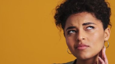 Ciddi bir Amerikalı kadının yakın plan görüntüsü stüdyodaki sarı duvarın arkasında tek başına durduğunu düşünüyor.