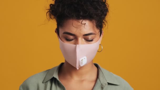 美しい自信に満ちたアメリカ人女性のクローズアップビューは スタジオで黄色の壁に隔離された顔の医療保護マスクを身に着けています — ストック動画