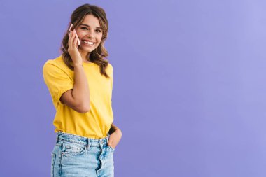 Mor arka planda izole bir şekilde cep telefonuyla konuşurken gülümseyen mutlu güzel kız.
