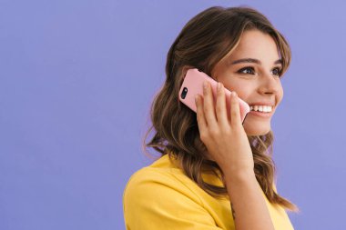 Mor arka planda izole bir şekilde cep telefonuyla konuşurken gülümseyen mutlu güzel kız.