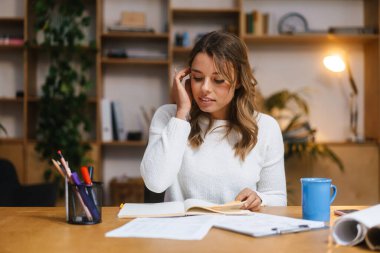 Ofis masasında otururken belgelerle çalışan genç ve güzel bir girişimci kadın.
