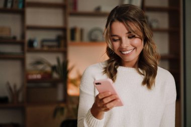 Modern ofiste otururken cep telefonu kullanan gülümseyen çekici bir kadının fotoğrafını çek.