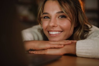 Kulaklıkla gülümseyen genç bir kadın dizüstü bilgisayarda webinar izliyor, bilgisayar eğitimi alıyor, arama yapıyor, çevrimiçi konferansa katılıyor, çevirmenlik eğitimi veriyor.