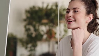 Mutlu kadının, monitöre ve ofiste otururken kameraya bakışının yan görüntüsü.