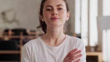 Ofiste kollarını kavuşturan tişörtlü gülümseyen kadın.