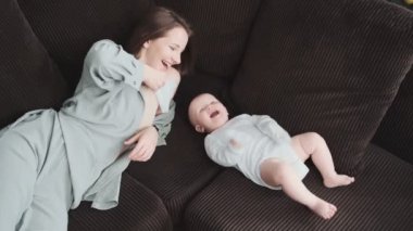 Gülümseyen anne kanepeye uzanmış bebeğiyle oynuyor.