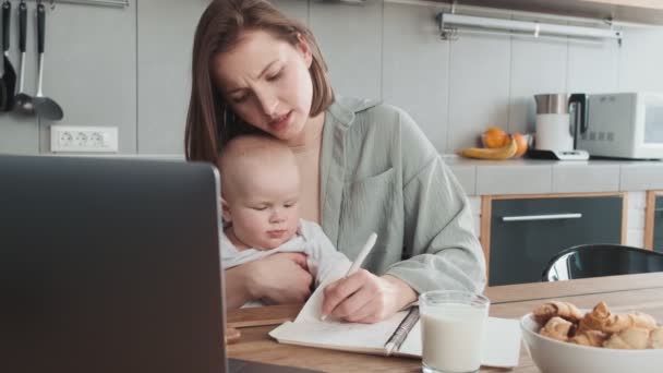 Tired Mom Writing Something Notebook Holding Her Little Child Her — Stock Video