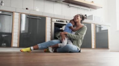 Gülümseyen Afrikalı bir ailenin anne ve kızının yerde otururken sarılıp öpüşmelerinin yan görüntüsü.