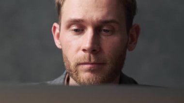 Gri bir ofiste dizüstü bilgisayara bakan pozitif bir adamın yakın çekimi.