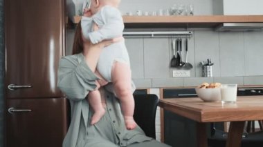 Mutfakta otururken küçük bebeğini kucaklayan gülümseyen bir anne.