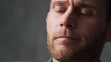 Gri bir ofiste sakalını ovuşturan dalgın bir adamın yakın plan fotoğrafı.