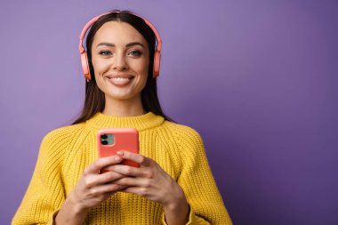 Kulaklık takan, elinde cep telefonu tutan mutlu genç bir kadın.