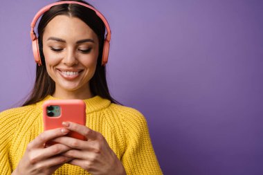 Kulaklık takan, elinde cep telefonu tutan mutlu genç bir kadın.
